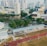 An aerial view of an urban area featuring a sports complex with a track field and a grandstand. Surrounding the sports area are numerous high-rise buildings, greenery, and roads with vehicles. The image captures people engaging in activities on the field.